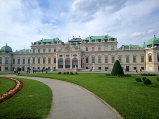 Fototapeta premium Vienna, Austria - August 15, 2019: View of the Belvedere Palace in Vienna, built in the Baroque style against the blue sky and clouds. People walk along the green lawns