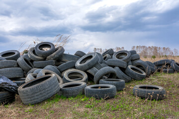 A large pile of old used car tires is located in a forest clearing. The problem of environmental...