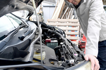 車の運転中にトラブルに遭いボンネットを開けるアジア人の男性
