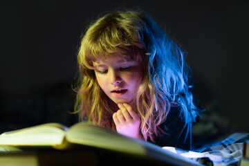 Child reading a book in bed before going to sleep. Little boy lying on bed reading book at home....