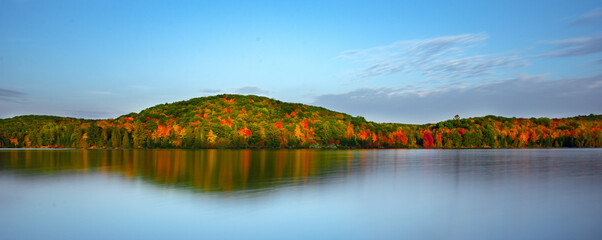 Autumn forest hills on the shore of lake in Gatineau Park, Canada. Reflections in still water. Peaceful autumn scenery