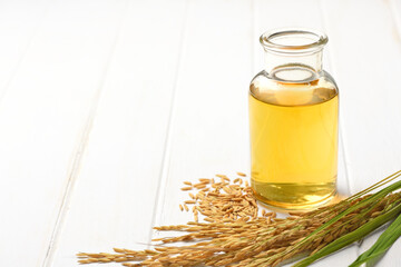 Rice bran oil with paddy rice and rice ears on white wood.
