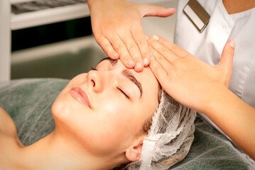 Head massage. Beautiful caucasian young white woman receiving a head and forehead massage with closed eyes in a spa salon