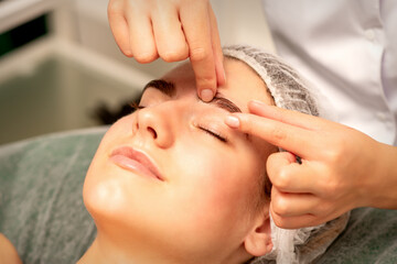 Eyebrow massage. Beautiful caucasian young white woman receiving an eye and eyebrow massage with closed eyes in a spa salon