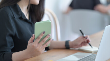 Close up view of businesswoman hand using mobile phone while working on laptop computer.