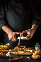 The chef peels raw potatoes in a restaurant kitchen before preparing a national dish. Close-up of a cook hands with a knife while working