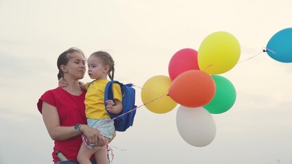 air holiday balloons for children holiday. happy family life. gel balls. mother carries little child kid daughter her arms. mom parent with baby girl outdoors. daughter hugs mom sitting arms embrace.