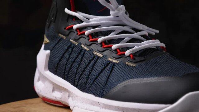 Close-up of a basketball sneaker on a wooden surface. Dark background. View of the front and outside of the shoe. Camera flying around. Parallax effect. Selective focus