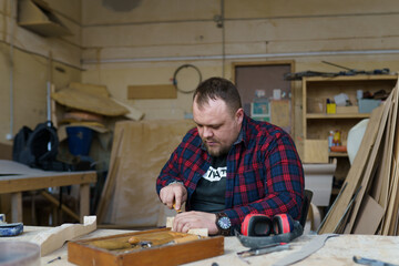 carpenter in a plaid shirt working with wood in the workshop