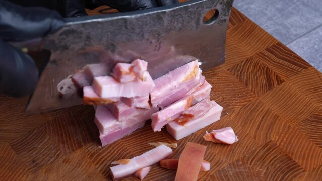 Closeup of chef cuts bacon guanciale into little cubes with old retro knife on wooden cutting board