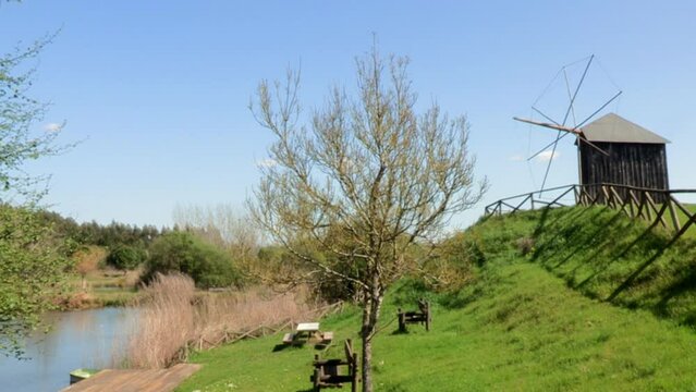 Image with windmill, lake and trees with blue sky in the background, on a sunny day.