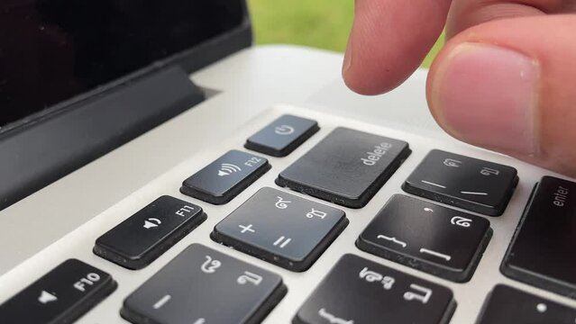 Typing on keyboard. Male hand finger press "delete" key button repeatedly on English - Thai laptop keyboard. Digital nomad professional hand on laptop close up - technology concept
