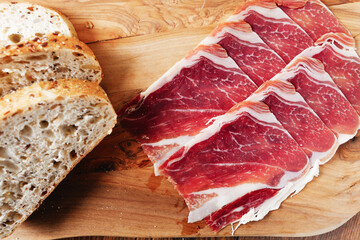 Premium Spanish dry cured ham on a wooden board and wooden background and a slice of bread . Top quality meat product.