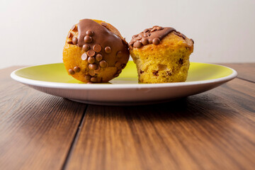 Two chocolate chip muffins on a yellow plate and wooden table . Copy space. Premium quality bakery product.