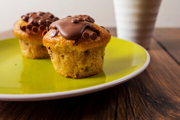 Two chocolate chip muffins on a yellow plate and white cup of tea and wooden table . Copy space. Premium quality bakery product.