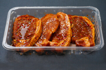 Fresh pork chops in Korean style marinade with spicy sous and herbs. Summer barbeque product in a plastic tray on dark surface. Meat industry. Orient inspired flavor. Close up