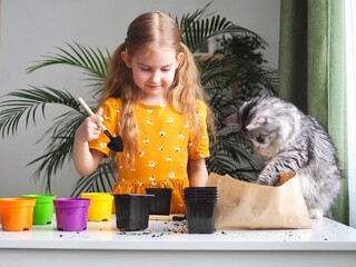 Little toddler girl planting seeds in the pots with cat. Love of pets. Funny and curious pets. Home gardening, transplanting plants, seedlings
