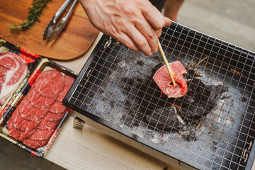 Young man use Chopstick grilling sliced meat on charcoal grill with Raw Beefs set on table during summer time.