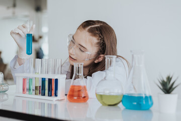 Caucasian girl student learning a chemical experiment in science class. Cute little girl holding test tube while learning chemistry class in white laboratory room.