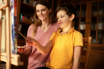 Mother and son painting at home. Little boy drawing with mom in living room.