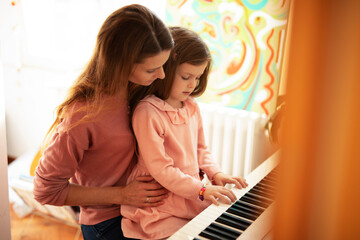 Woman and girl playing a piano. Beautiful mom teaching her daughter playing a piano...