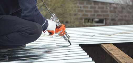Worker using glue gun with adhesive to fix the metal steel on the roof. - obrazy, fototapety, plakaty