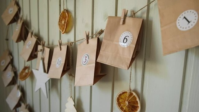 Advent calendar. Small handmade paper gifts hanging on the background of wooden wall, close up. Christmas Calendar, gift for children. DIY. Sustainable Christmas. Celebrating at home, childhood.