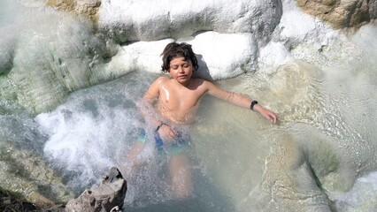 Boy 7child 7 years old relax in Bagni San Filippo natural bath in tuscany, Italy. sulphurous water and therapy for respiratory problems in children thermal baths, Siena ,Tuscany - obrazy, fototapety, plakaty