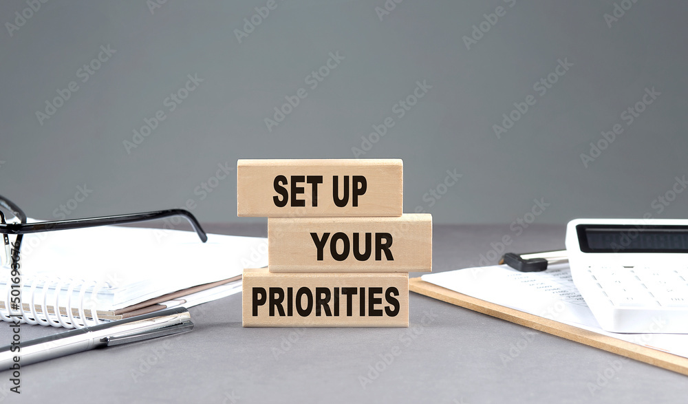 Poster set up your priorities text on wooden block with notebook,chart and calculator, grey background
