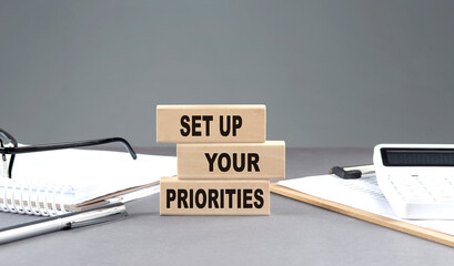 SET UP YOUR PRIORITIES text on wooden block with notebook,chart and calculator, grey background