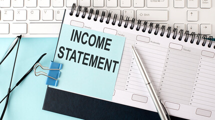 INCOME STATEMENT text on blue sticker on the planning and keyboard,blue background