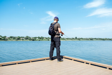 Fisherman with spinning rod on the lake. fisherman with spinning in his hands catching fish at sun day. Fisherman with rod, spinning reel on the river bank.