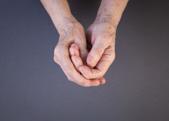 Hands of an elderly woman rubbing her sore fingers on a gray background. Arthritis Awareness Month concept.