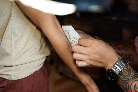 Close-up view of unrecognizable tattooist transferring tattoo image onto hand of his customer from a piece of paper