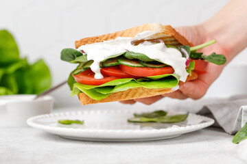 Vegetable vegan sandwich with white sauce, tomato, spinach, cucumber. Woman hand taking toast.