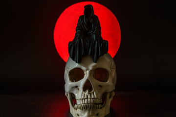 A statue of a grim reaper sitting on a skull on a full moon background.