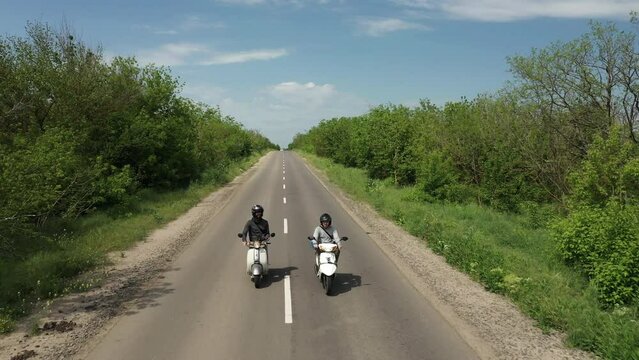 front drone shot two scooter drivers rides on an highway road in summer