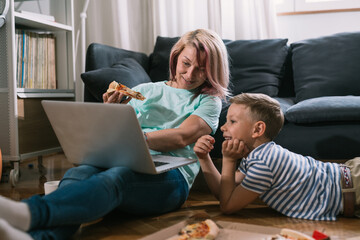 single mother and son enjoying time together at home, using laptop computer and eating pizza