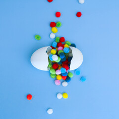 Colored round pom-poms spilling out of a white broken egg, funny egg
