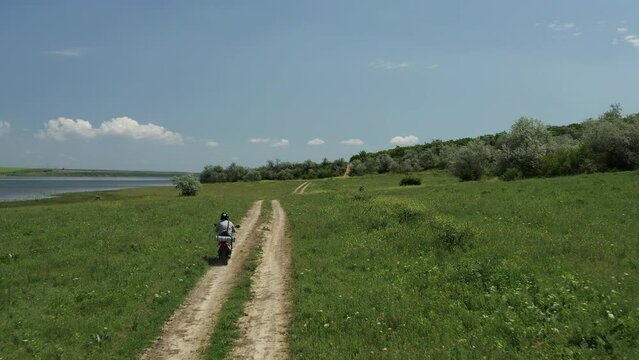 Young male rides moped motorbike on dirt country road at summer drone shot