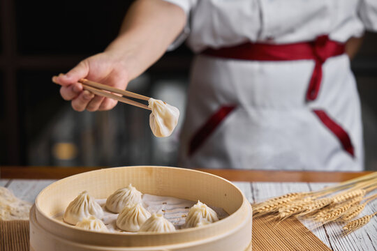 Close up of Chinese steamed Xiaolongbao held in chopsticks, being taken out of bamboo steamer with rustic wood.