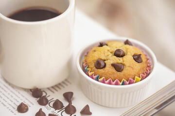Black coffee and fresh homemade banana muffin decorated with chocolate chips on the table