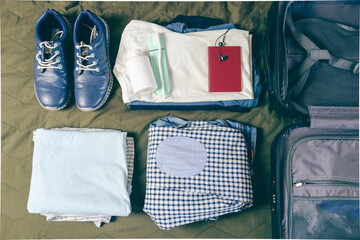 Stacked clothes, a passport, a pair of shoes, and a toothbrush next to an open suitcase. Top view...