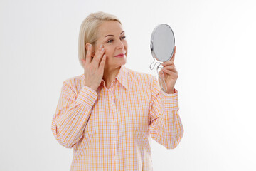 Happy Middle aged Woman looking in mirror on her face with wrinkles on the forehead and wrinkle...