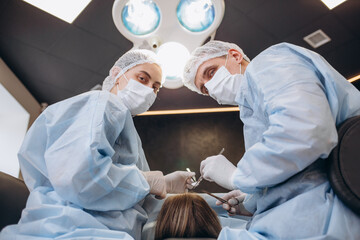 Surgeon performing cosmetic surgery on breasts in hospital operating room. Surgeon in mask wearing...