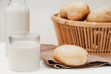 alternative non dairy milk, potato milk in a glass and potatoes on a table in a basket. lactose free drink, homemade fresh beverage for healthy lifestyle