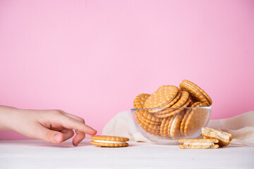 The child's hand takes a cookie from a glass bowl on a pink background. The concept of breakfast and a quick snack.