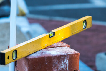 yellow spirit level on a pile of red bricks which are being used for paving and repair of a...