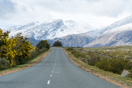 asphalt or tarred empty road leading into snow covered mountains in Ceres, Western Cape, South Africa during winter season