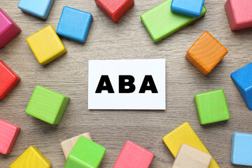 Colorful building blocks and card with abbreviation ABA on wooden table, flat lay